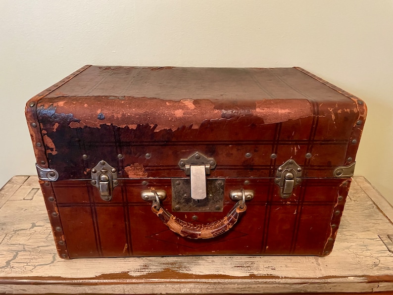 May include: A vintage brown leather suitcase with metal clasps and a leather handle. The suitcase has a worn and distressed look, with some of the leather peeling off.