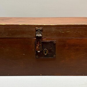May include: A rectangular wooden chest with a hinged lid and a metal clasp. The chest is stained a dark brown color, with visible wood grain. The metal clasp and keyhole plate show signs of age and wear.