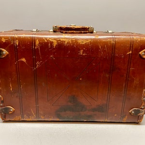 May include: A vintage brown leather suitcase with a decorative cross pattern and metal accents. The suitcase has a worn and weathered look, suggesting it has been well-traveled.
