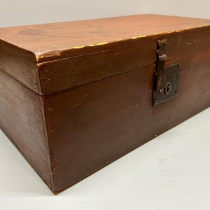 May include: A rectangular wooden box with a hinged lid, painted in a dark brown color. The box features a metal latch and keyhole on the front. The wood shows signs of wear, with some paint chipping.