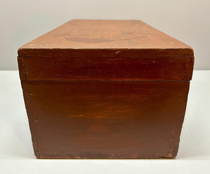 May include: A rectangular wooden box with a hinged lid. The box is stained a dark reddish-brown color, with visible wood grain and some wear. The box appears to be vintage or antique, and is likely used for storage or display.