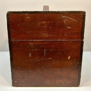 May include: A vintage wooden box with a dark brown finish and a leather handle. The box has a rectangular shape with a hinged lid and appears to be well-worn, showing signs of age and use. The edges are framed with a darker material.