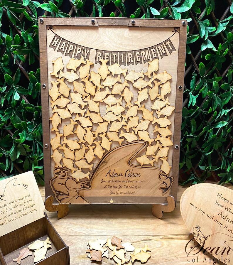 May include: A wooden retirement sign with a fish theme. The sign has a cutout of a fisherman holding a fishing rod and a shark fin. The sign says "Happy Retirement" and "Adam Cohen, Your dedication and perseverance set the bar for the rest of us. You'll be missed."