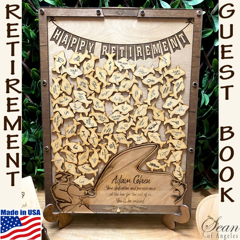 May include: A wooden guest book with a shark fin design and the text "Happy Retirement" and "Adam Cohen". The book is filled with small wooden fish with signatures on them. The book is made in the USA.