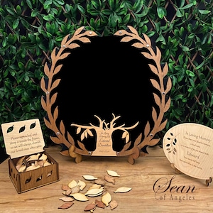 May include: A wooden memorial tree frame with a black background and a tree with leaves. The frame is surrounded by a wreath of leaves. There is a small wooden box with leaves inside and a sign that says "Please sign a leaf and drop it inside the frame, so we will always cherish our loved ones who came." There is also a small wooden plaque with the text "In Loving Memory of Edward Dandelion 1940-2024".