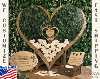 May include: A wooden heart-shaped guest book with a clear acrylic center. The frame holds small wooden hearts for guests to sign. Includes a wooden box and sign with instructions. The text says "Brandon & Morgan".