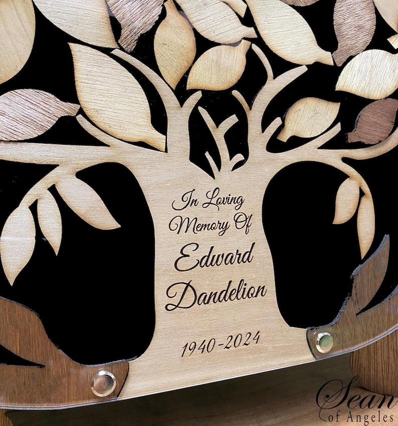 May include: A wooden tree of life memorial plaque with a black background. The plaque is engraved with the text "In Loving Memory Of Edward Dandelion 1940-2024".