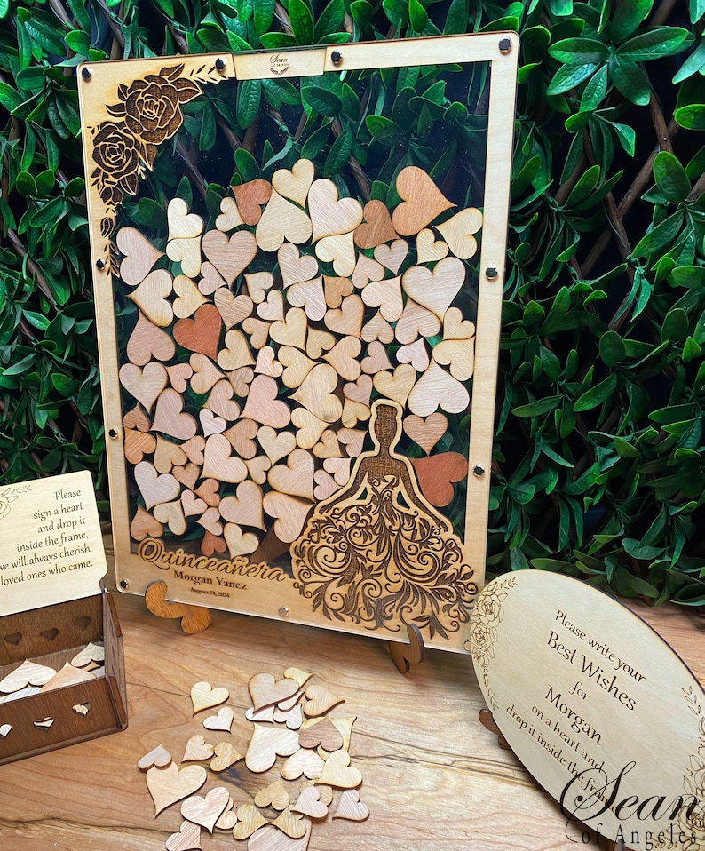 May include: Wooden Quincea&ntilde;era guest book with a frame filled with heart-shaped pieces. The frame has a laser-cut design of a woman in a dress and the text "Quincea&ntilde;era". Includes a wooden box and a sign with text.