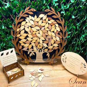 May include: A wooden tree-shaped memorial guest book with a black background and a clear acrylic frame. The tree has many leaves that can be signed by guests. The leaves are made of wood and come in a small wooden box. The guest book also includes a small wooden plaque with the text "In Loving Memory of Edward Dandelion 1941-2023".