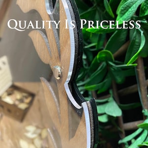 May include: A wooden sign with a leafy design and the text "QUALITY IS PRICELESS". The sign is framed with a black border and a silver trim.