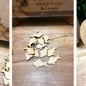 May include: Wooden guest book with a fishing theme. Guests write their best wishes on wooden fish-shaped chips and drop them into a box. The sign reads "Please write your best wishes for Adam on a chip and drop it inside the frame."