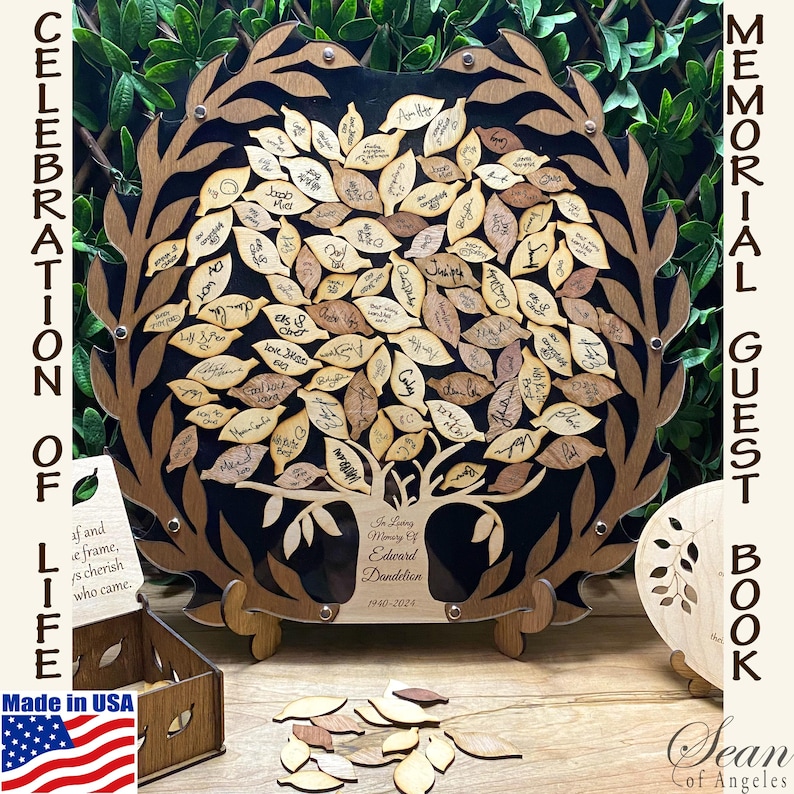 May include: A wooden memorial guest book shaped like a tree with leaves that can be signed by guests. The leaves are attached to the tree with a small pin. The tree is on a black background with a wooden frame. The text "In Loving Memory of Edward Dandelion 1940-2024" is engraved on the tree trunk. The guest book is made in the USA.