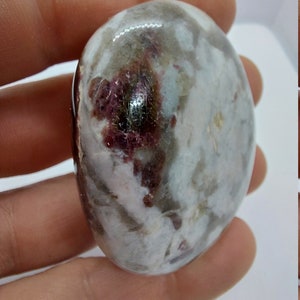 May include: A white and grey tumbled stone with red and pink inclusions. The stone is smooth and polished.