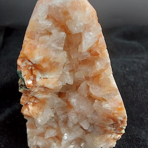 Op de afbeelding: Een natuurlijke kristalformatie met een ruw, getextureerd oppervlak. Het kristal heeft een mix van perzik-, oranje- en wittinten, met zichtbare kristallijne structuren. De algemene vorm is onregelmatig en toont de natuurlijke schoonheid van het mineraal.