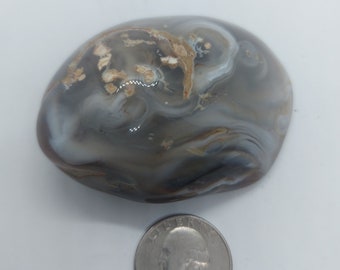 May include: A smooth, gray agate stone with white and brown swirling patterns. The stone is about the size of a US quarter.