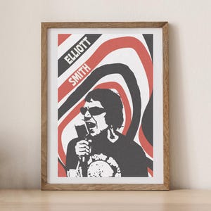 Puede incluir: Lámina artística enmarcada con una ilustración en blanco y negro de un cantante con gafas de sol sosteniendo un micrófono. El fondo tiene líneas onduladas rojas, negras y blancas. El nombre "ELLIOTT SMITH" está impreso en rojo y negro.