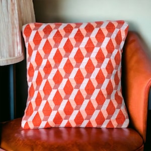 Puede incluir: Un coj&iacute;n de decoraci&oacute;n rojo y blanco con un patr&oacute;n geom&eacute;trico de rombos. El coj&iacute;n est&aacute; sobre una silla de cuero marr&oacute;n.