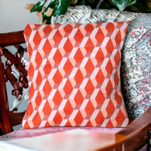 Puede incluir: Un coj&iacute;n de decoraci&oacute;n rojo y blanco con un patr&oacute;n geom&eacute;trico de rombos. El coj&iacute;n est&aacute; sobre una silla de terciopelo rosa.