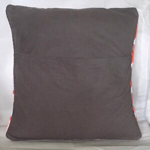 Puede incluir: Una almohada gris con un patr&oacute;n geom&eacute;trico blanco y naranja en la parte posterior. La almohada est&aacute; hecha de una tela suave y mullida.