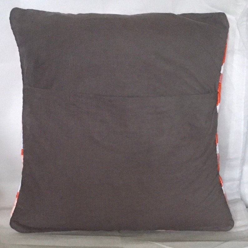 Puede incluir: Una almohada gris con un patr&oacute;n geom&eacute;trico blanco y naranja en la parte posterior. La almohada est&aacute; hecha de una tela suave y mullida.