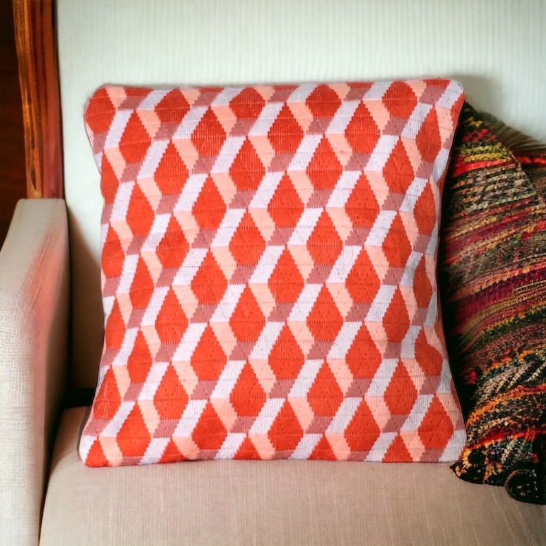Puede incluir: Una almohada de tiro roja y blanca con un patr&oacute;n geom&eacute;trico de diamantes. La almohada est&aacute; en un sof&aacute; beige claro.