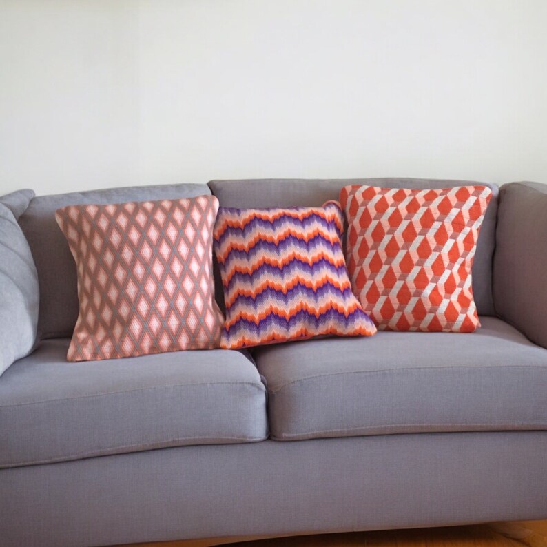 Puede incluir: Tres cojines decorativos sobre un sof&aacute; gris. Los cojines tienen patrones geom&eacute;tricos en tonos de rosa, naranja y morado.