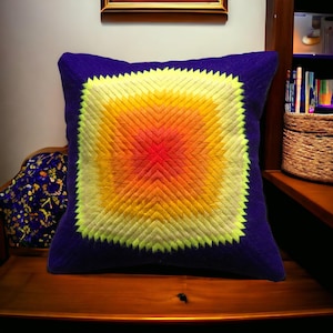 May include: A square throw pillow with a vibrant yellow, orange, and red geometric pattern on a deep blue background.