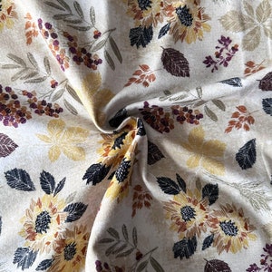 May include: Beige fabric with a repeating pattern of sunflowers, leaves, and berries. The sunflowers are yellow with black centers and the leaves are green and brown. The berries are purple and red.