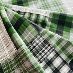 以下が含まれることがあります： 緑、グレー、黒、白の色合いのチェック柄のパッチワーク生地のクローズアップ。 生地は折りたたまれており、チェック柄のさまざまなセクションを示しています。 生地は綿のようです。