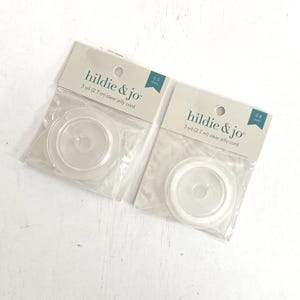 以下が含まれることがあります： hildie & jo の透明なゼリーコードの2つのパッケージ。各パッケージには、透明なコードのスプールが入っており、パッケージには「hildie & jo」と「3 yd（2.7 m）clear jelly cord」と書かれています。1つのパッケージは0.5 mm、もう1つは0.8 mmと表示されています。