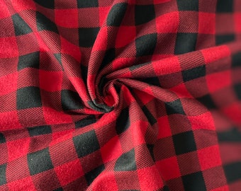 May include: Red and black buffalo plaid fabric with a soft, fuzzy texture. The fabric is folded and twisted, showing the pattern and texture.