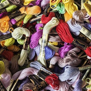 May include: A collection of embroidery floss spools in various colors, including red, orange, yellow, green, blue, purple, pink, brown, and gray. The spools are labeled with numbers.