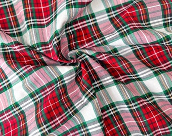 May include: A fabric featuring a classic plaid pattern with intersecting lines in red, dark green, and white. The textile is gathered in soft folds, creating a textured surface that highlights the repeating geometric grid of the tartan design.