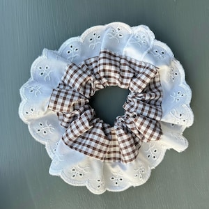 Könnte beinhalten: Ein braunes und weißes Gingham-Haargummi mit weißer Spitzenborte.