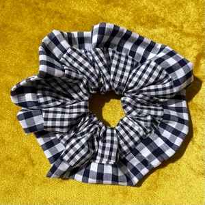 Könnte beinhalten: Ein schwarzer und weißer Gingham-Haargummi. Der Haargummi besteht aus zwei Stofflagen, wobei die obere Lage ein kleineres Gingham-Muster hat als die untere Lage.