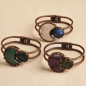 Puede incluir: Tres pulseras de alambre de cobre con un diseño de media luna. Cada pulsera presenta una gema diferente: blanca, verde y morada.