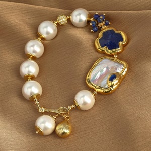 May include: A gold bracelet with white pearls, blue and white stones, and a gold charm. The bracelet has a delicate design and is perfect for adding a touch of elegance to any outfit.