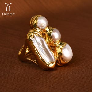 Puede incluir: Un anillo de oro con tres grandes perlas blancas engastadas en un diseño de oro texturizado.