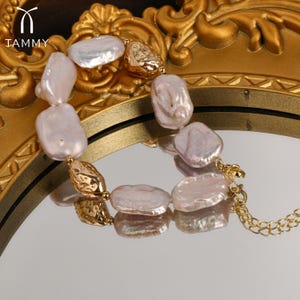 May include: A gold chain bracelet with a series of large, irregular, pale pink pearl beads. The bracelet has a clasp closure.