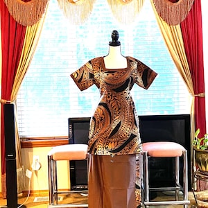 May include: A two-piece outfit consisting of a short-sleeved tunic and a long skirt. The tunic features a square neckline and a brown and black tribal-inspired geometric pattern. The skirt is a solid brown color with a matching patterned side panel.