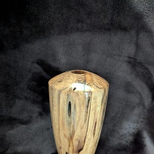 May include: A wooden vase with a unique, natural wood grain pattern. The vase is a light brown color with dark brown streaks throughout. It has a rounded, oval shape and a smooth, polished finish.