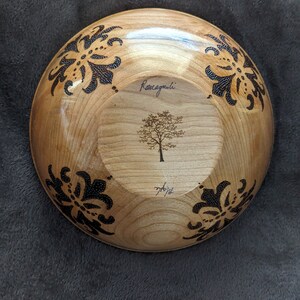 May include: A wooden bowl with a black floral design and a tree etched in the center. The bowl is signed "Ronagnoli" and dated "7/6/14".