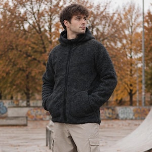 Könnte beinhalten: Eine dunkel anthrazitfarbene Kapuzenjacke mit Reißverschluss und texturierter Fleece-Optik, kombiniert mit einer locker sitzenden beigen Cargohose mit Seitentaschen und schlichten weißen Sneakern für ein funktionales, mehrlagiges Outfit.