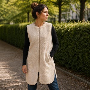Può includere: Un gilet lungo senza maniche in pile sherpa color crema, dotato di chiusura frontale con zip, scollo rotondo e due tasche laterali. Il capo presenta un esterno testurizzato e soffice, con un orlo dritto e spacchi laterali arrotondati.