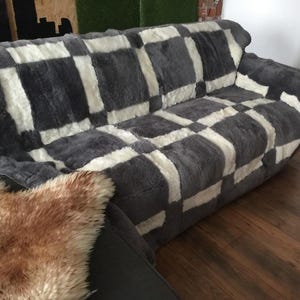 May include: A grey and white checkered sheepskin throw blanket on a sofa. The blanket is soft and fluffy, and it would be perfect for adding warmth and comfort to any room.