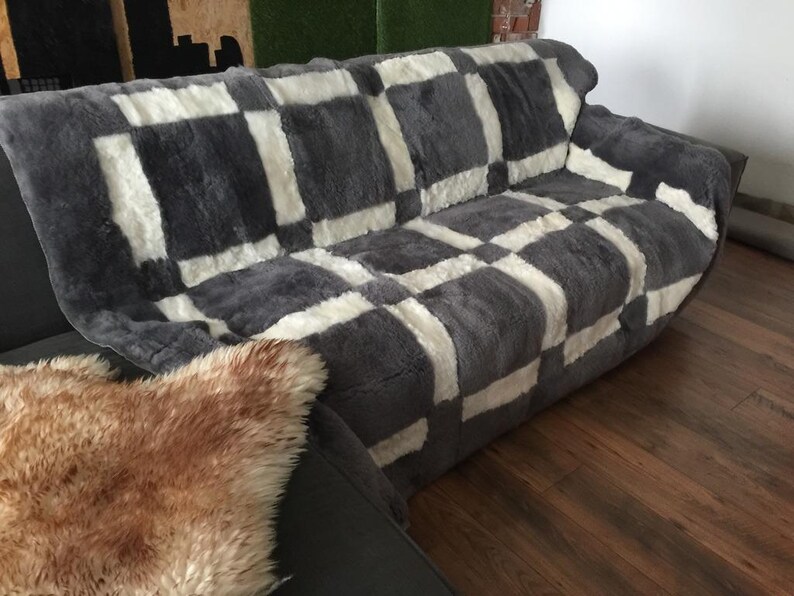 May include: A grey and white checkered sheepskin throw blanket on a sofa. The blanket is soft and fluffy, and it would be perfect for adding warmth and comfort to any room.