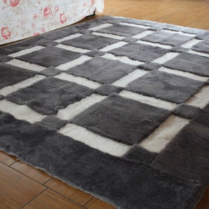 May include: A grey and white checkered rug with a soft, fluffy texture. The rug has a geometric pattern with squares of grey and white.