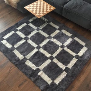 May include: A grey and white chequered rug with a soft, fluffy texture. The rug is made of sheepskin and has a modern design.