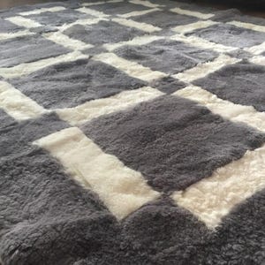 May include: A grey and white sheepskin rug with a chequered pattern. The rug is made of soft, fluffy sheepskin and has a luxurious feel.