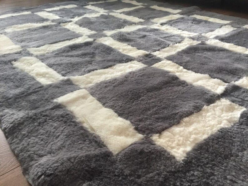 May include: A grey and white sheepskin rug with a chequered pattern. The rug is made of soft, fluffy sheepskin and has a luxurious feel.
